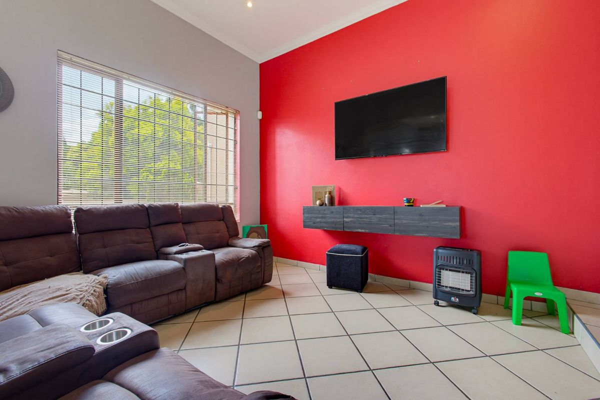 A living room featuring tiled flooring, a floating media console, and large windows with venetian blinds, finished with a bold red accent wall.