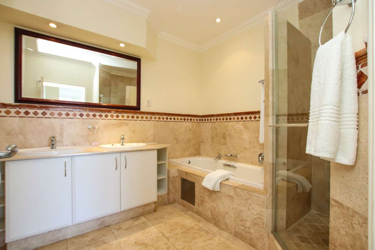 A spacious bathroom featuring a double vanity with white cabinetry, a built-in bathtub, and a separate glass-enclosed shower with natural stone tiling.