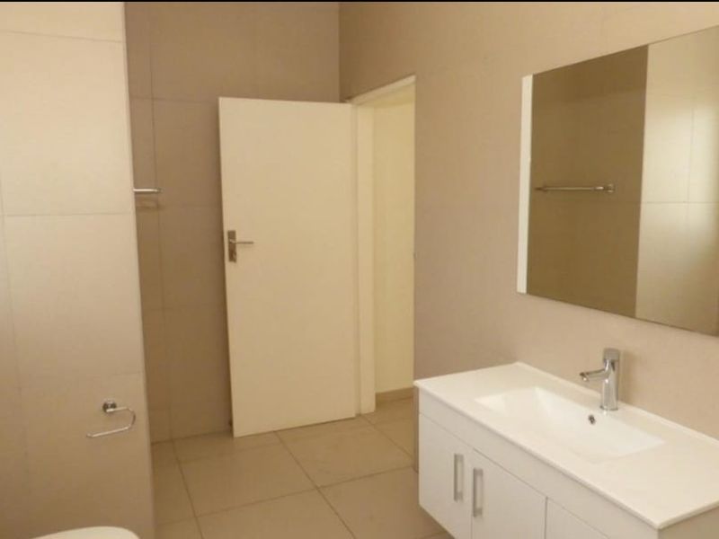 A clean, modern bathroom featuring a vanity cabinet with a basin, wall-mounted mirror, and neutral floor-to-ceiling tiling.