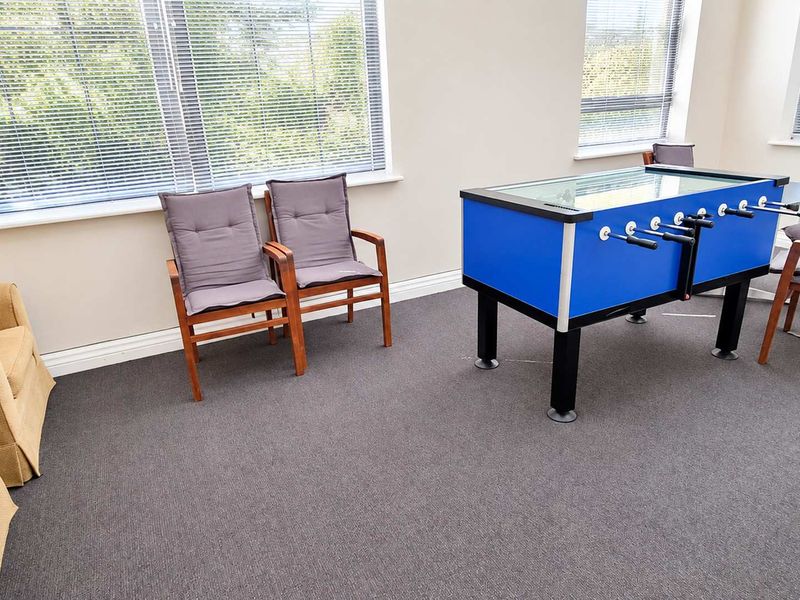 A bright office space featuring neutral walls, grey carpeting, and large windows with fitted venetian blinds, suitable for a professional work or breakout area.