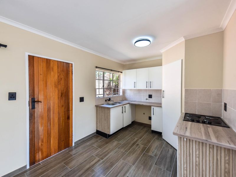 A clean, functional kitchen featuring modern cabinetry, wood-look tiled flooring, a built-in hob, and a solid timber door leading to the exterior.