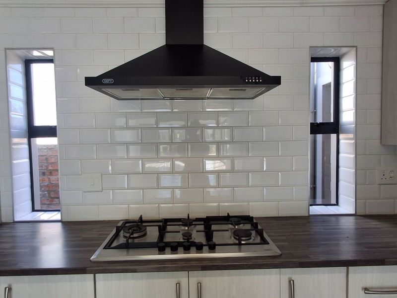 Modern kitchen featuring a gas hob, black extractor fan, white subway tile backsplash, and dark laminate countertops with ample built-in cabinetry.