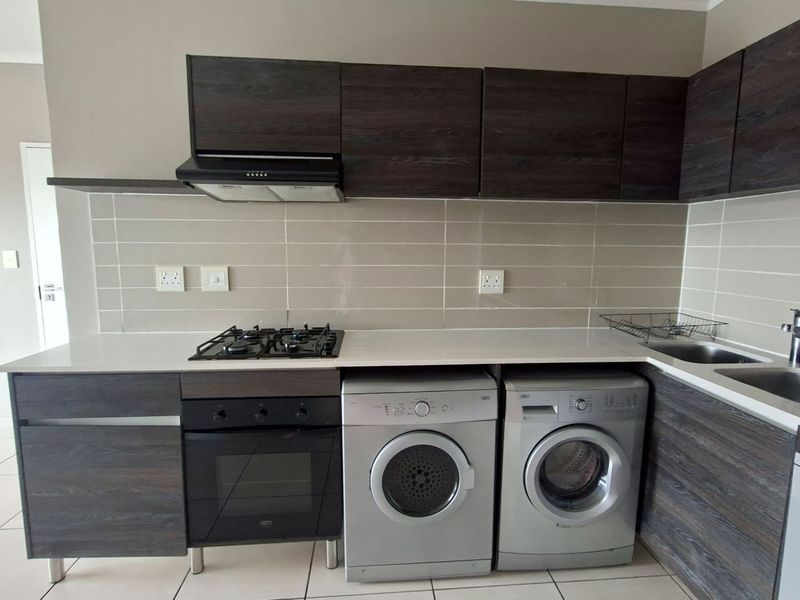 Modern kitchen featuring dark wood cabinetry, stone countertops, subway tile backsplash, integrated gas hob, electric oven, and dedicated space for laundry appliances.