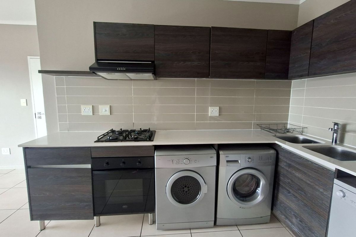 Modern kitchen featuring dark wood cabinetry, stone countertops, subway tile backsplash, integrated gas hob, electric oven, and dedicated space for laundry appliances.