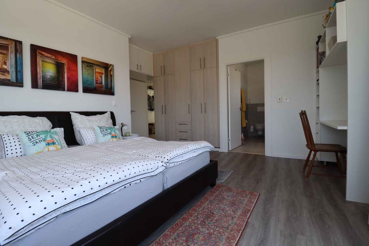 Spacious bedroom featuring light wood-finish built-in cupboards, laminate flooring, and an integrated desk area with direct access to an en-suite bathroom.