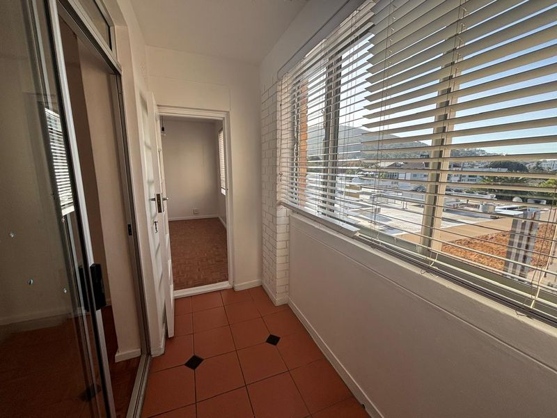 Enclosed balcony area featuring tiled flooring, a brick feature wall, and venetian blinds, offering an elevated view of the surrounding neighborhood.