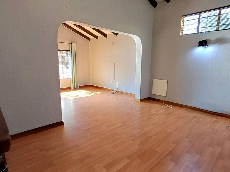 Spacious living area featuring laminate flooring, exposed timber ceiling beams, and an arched transition to an adjoining room with natural light.