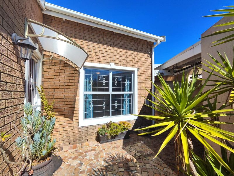 A well-maintained brick exterior rear courtyard featuring paved flooring, a protective awning over the entrance, and secure window bars.