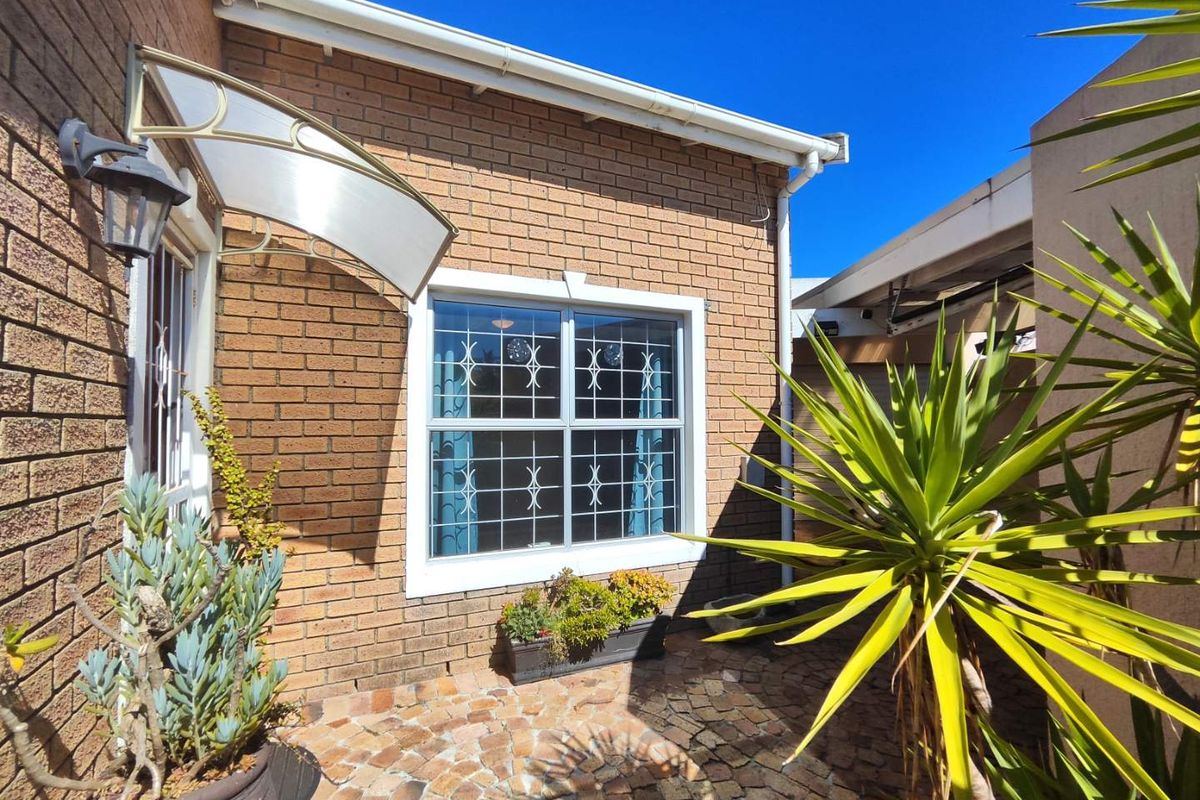 A well-maintained brick exterior rear courtyard featuring paved flooring, a protective awning over the entrance, and secure window bars.