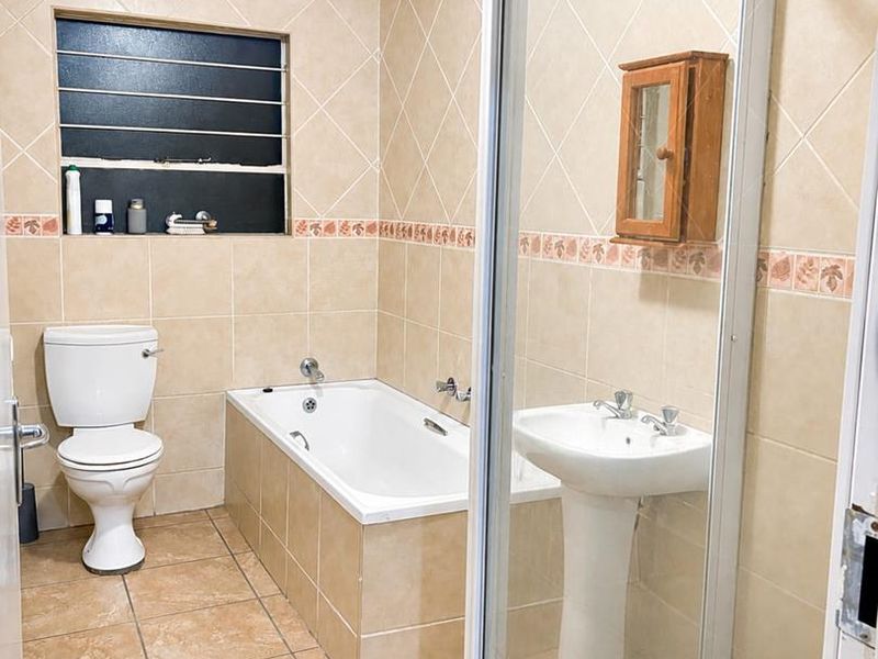 A functional bathroom featuring a pedestal basin, built-in bathtub, separate shower enclosure, and neutral tiled finishes throughout.