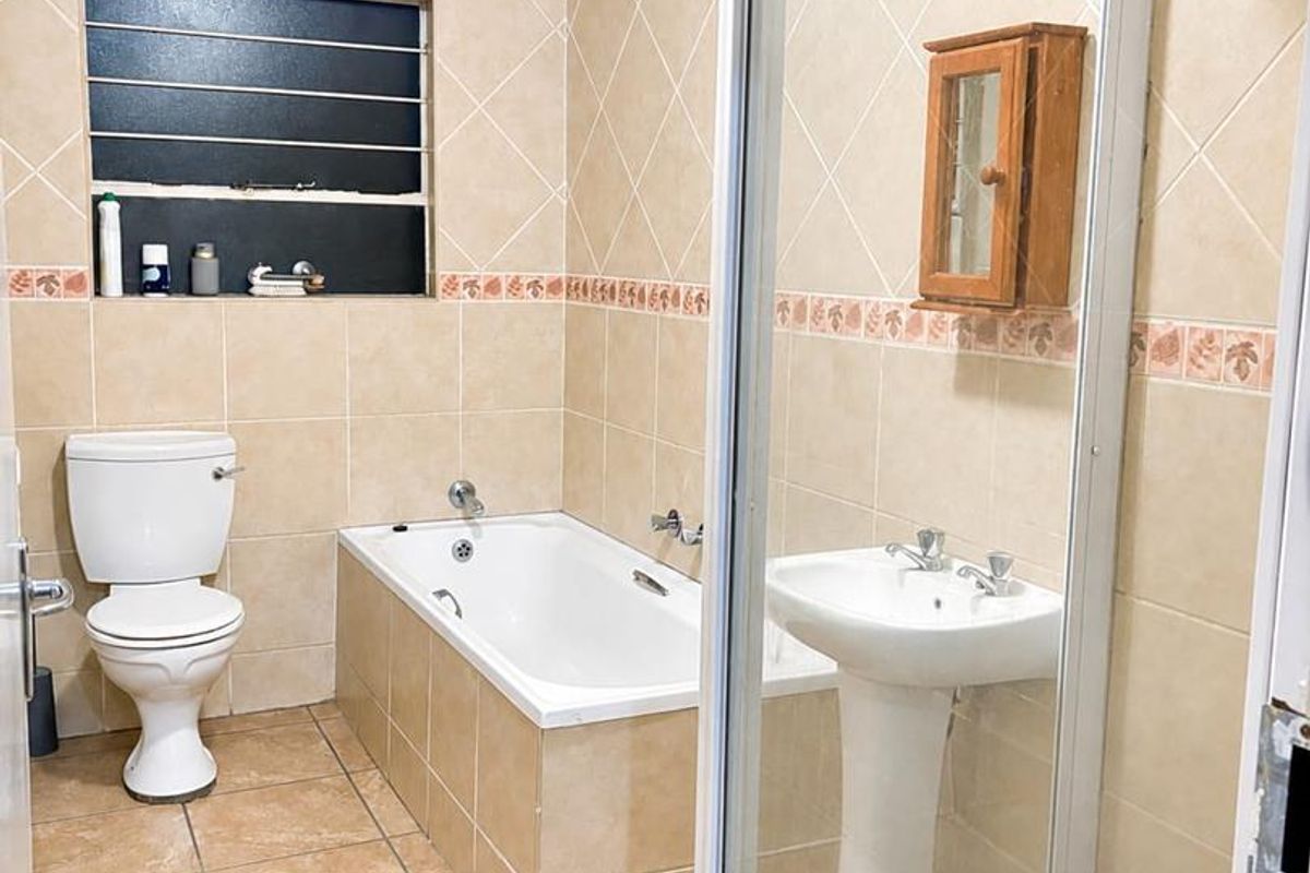 A functional bathroom featuring a pedestal basin, built-in bathtub, separate shower enclosure, and neutral tiled finishes throughout.