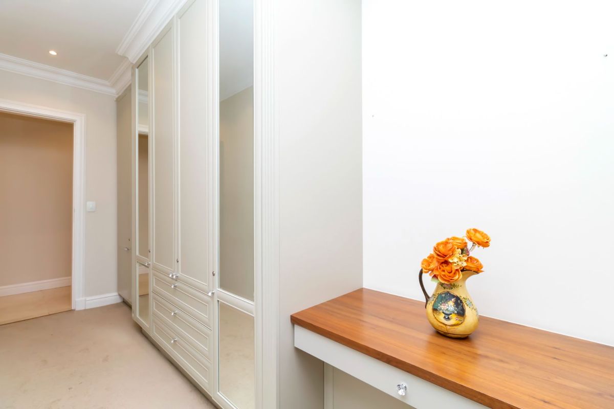 A well-maintained dressing area featuring extensive built-in cabinetry with mirrored panels and a sleek wooden vanity surface.