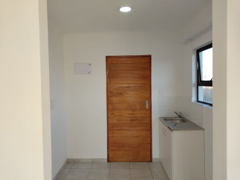 A clean and functional laundry area featuring a stainless steel sink, built-in cabinetry, tiled flooring, and a solid timber door.