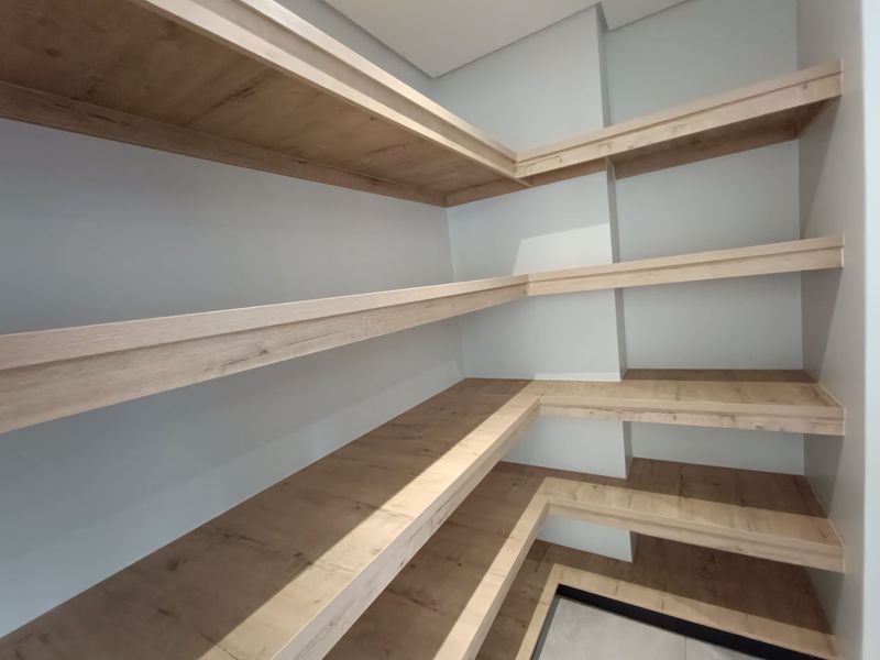 A clean, modern walk-in pantry or scullery storage area featuring extensive built-in timber-look shelving.