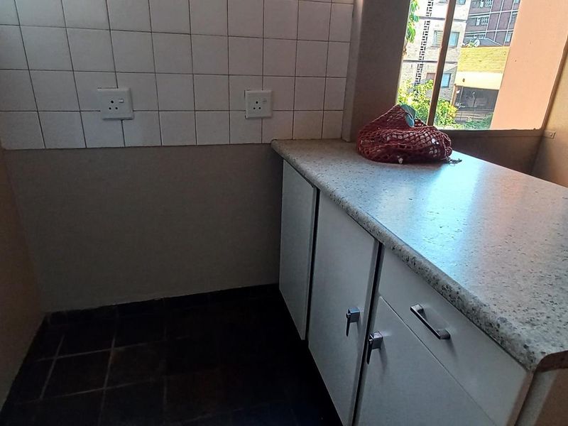 A functional kitchen area featuring built-in cabinetry, a laminate countertop, and a tiled backsplash, providing a practical space for food preparation.