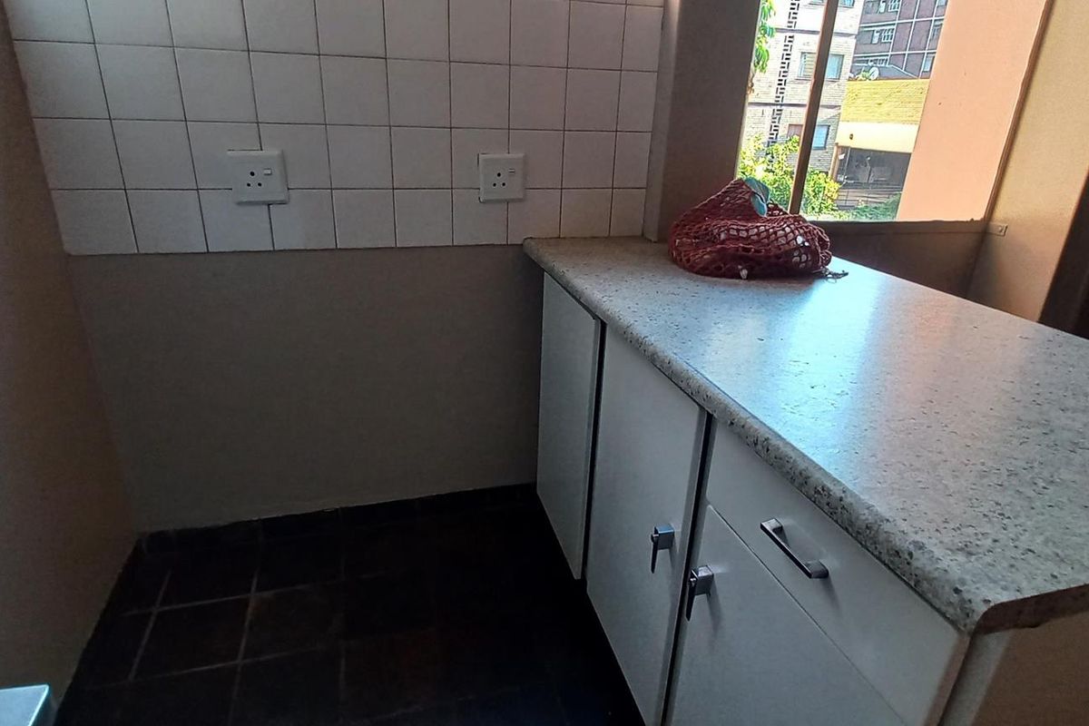 A functional kitchen area featuring built-in cabinetry, a laminate countertop, and a tiled backsplash, providing a practical space for food preparation.