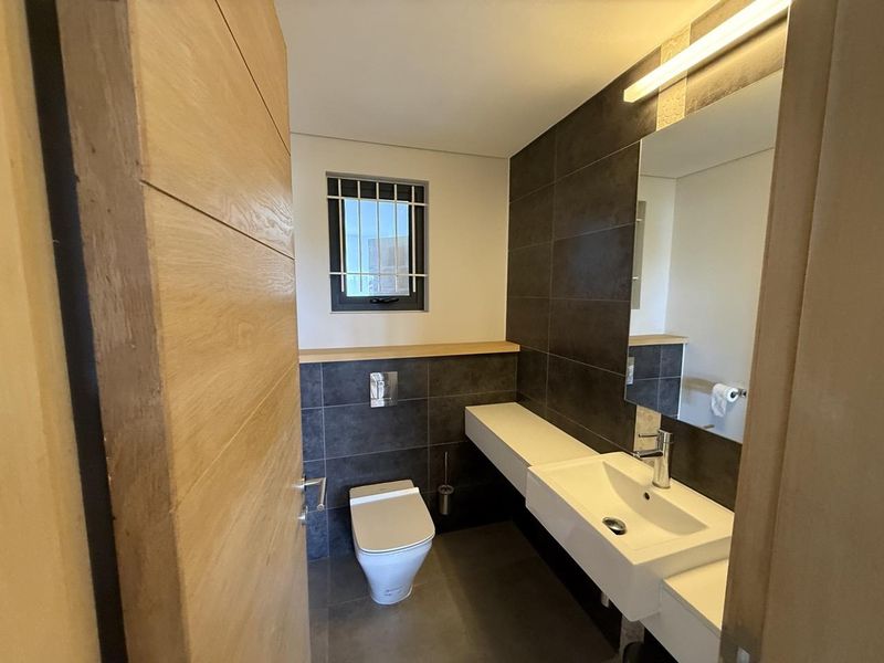 Modern guest bathroom featuring a wall-hung toilet, floating vanity with basin, and dark tiled feature wall.