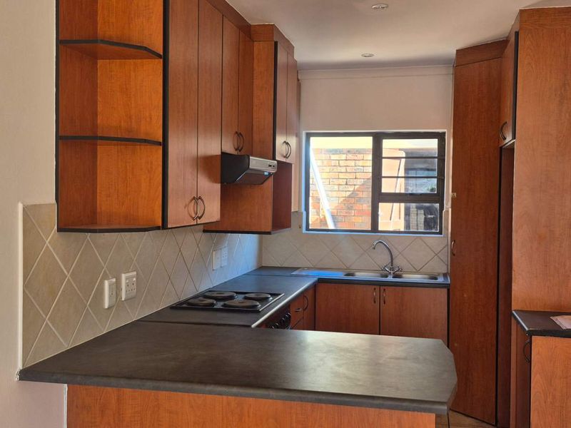 A functional kitchen featuring wood-look laminate cabinetry, dark countertops, a built-in hob with extractor fan, and a tiled backsplash.