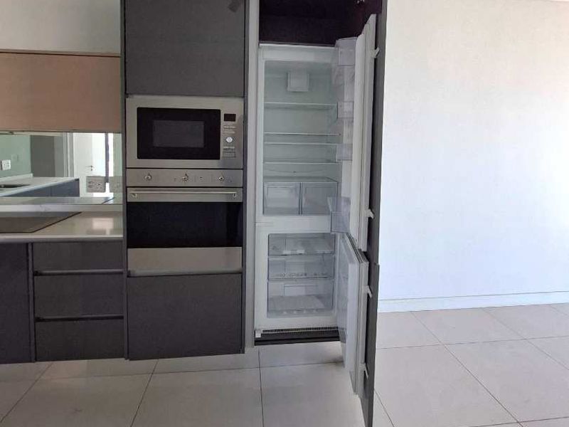 Modern kitchen featuring sleek dark cabinetry, integrated appliances including an oven, microwave, and fridge-freezer, complemented by neutral tiled flooring.