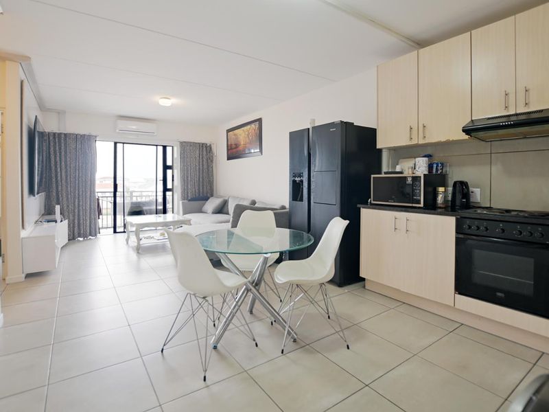 Open-plan living area featuring a functional kitchen with built-in cabinetry, oven, and hob, flowing into a lounge space with access to a balcony.