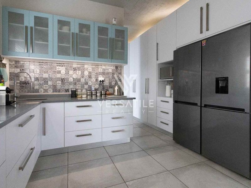 Modern kitchen featuring white and light blue cabinetry, stone countertops, a decorative tiled backsplash, and integrated storage solutions.