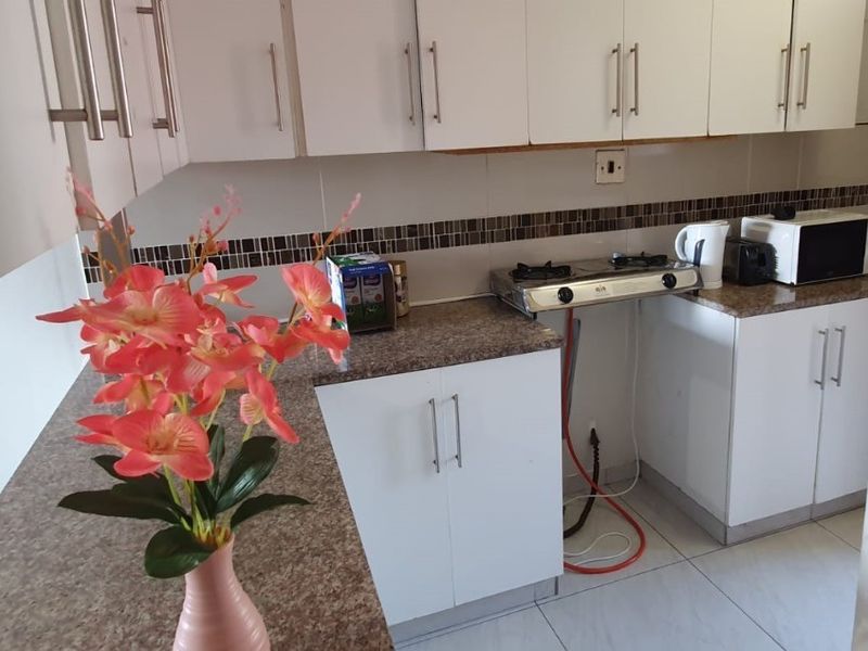 A compact kitchen featuring white cabinetry, granite-look laminate countertops, a gas hob, and a decorative tiled backsplash.