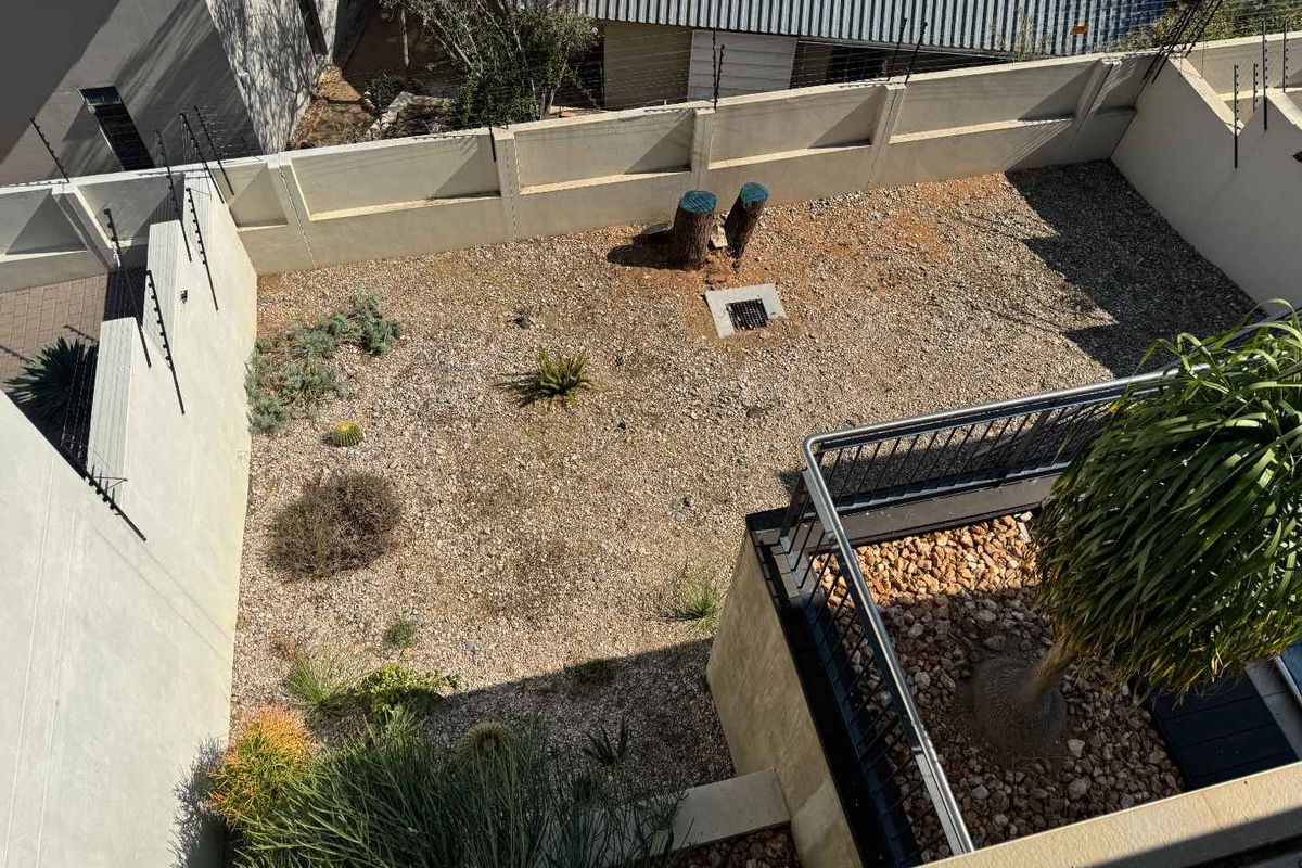 An elevated view of a private rear courtyard featuring a gravel-covered garden area, perimeter boundary walls with security fencing, and a small balcony section.