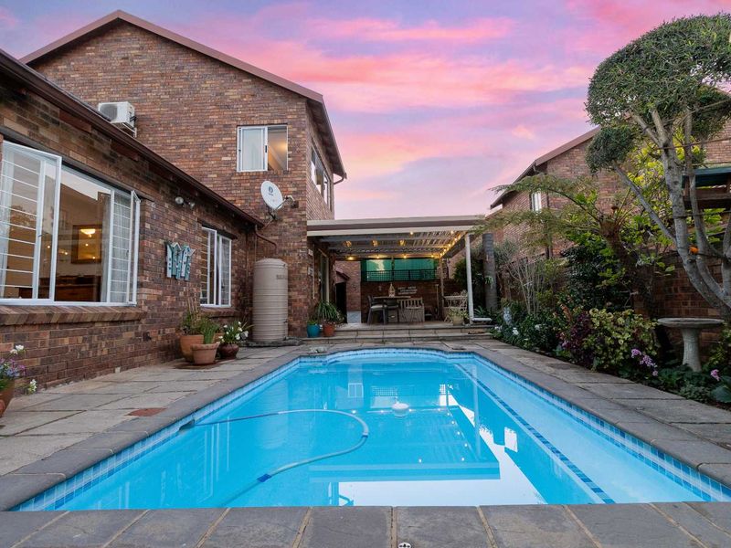 A well-maintained townhouse backyard featuring a swimming pool, paved surround, and a covered patio area set against a classic brick exterior.