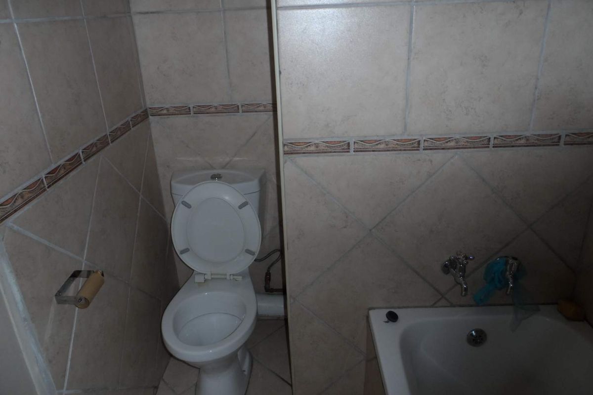 A dated bathroom featuring ceramic wall and floor tiles, a standard toilet, and a bathtub with exposed plumbing fixtures.
