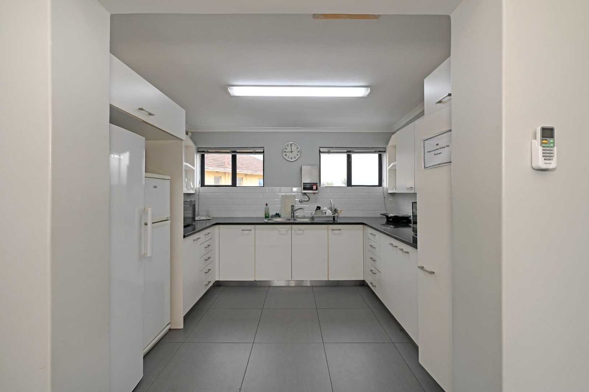 A functional kitchen featuring white cabinetry, dark countertops, tiled backsplash, and grey floor tiles, providing a clean and practical workspace.