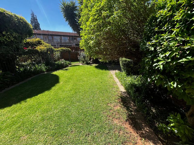 A well-maintained private garden featuring a lush green lawn, mature trees, and secure perimeter fencing.