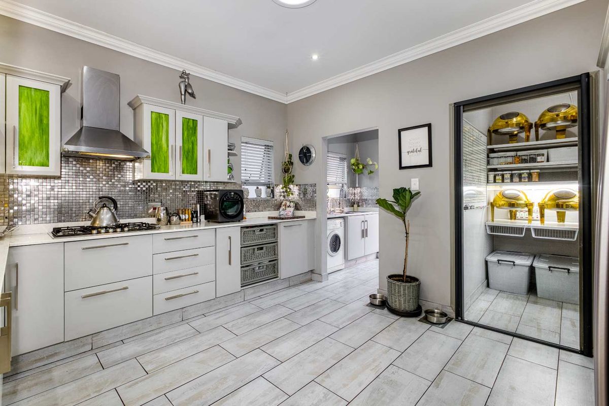 Modern kitchen featuring white cabinetry, mosaic tile backsplash, stainless steel extractor fan, gas hob, and an adjacent scullery with laundry facilities.