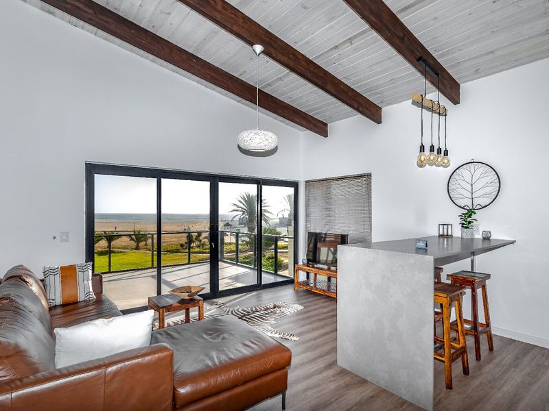Modern open-plan living area featuring exposed timber ceiling beams, sleek breakfast bar, and large sliding doors opening to a scenic balcony.