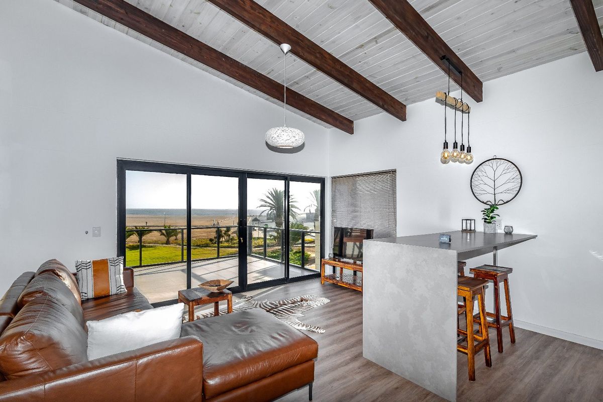 Modern open-plan living area featuring exposed timber ceiling beams, sleek breakfast bar, and large sliding doors opening to a scenic balcony.