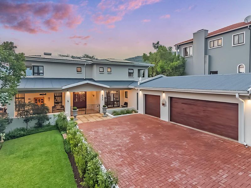 A well-maintained double-story residence featuring a paved driveway, double garage, covered entrance, and landscaped front garden at dusk.