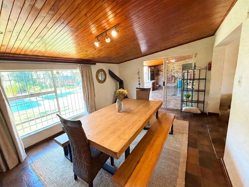Dining room featuring a warm timber-clad vaulted ceiling, terracotta floor tiles, and large windows with security bars overlooking the pool area.
