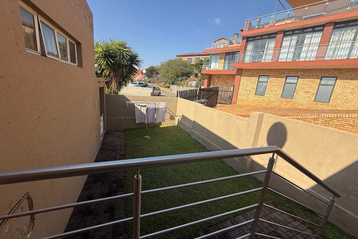 A rear exterior view showing a small private garden area with a paved walkway, lawn, and stainless steel balustrade overlooking the space.