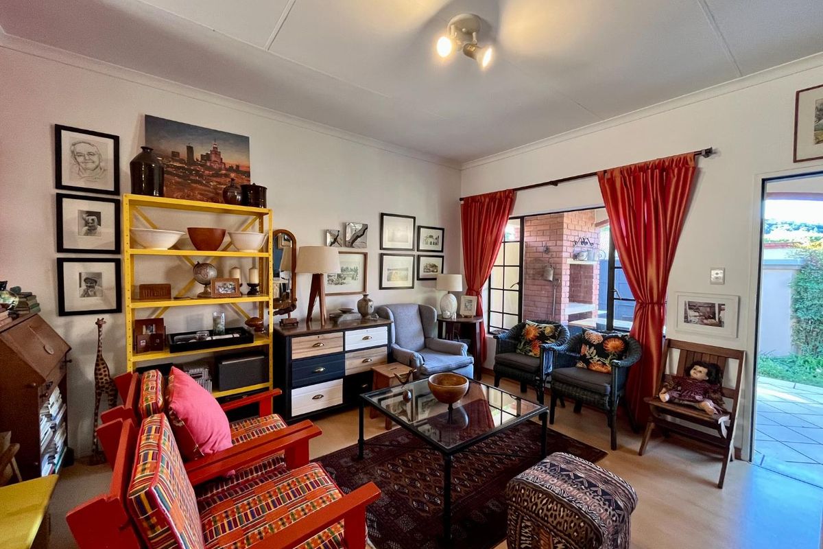 A cozy living room featuring tiled flooring, a ceiling-mounted spotlight fixture, and large windows with direct access to an outdoor patio area.