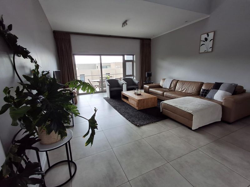 Spacious living room featuring large format floor tiles and a wide sliding glass door providing access to an outdoor balcony area.