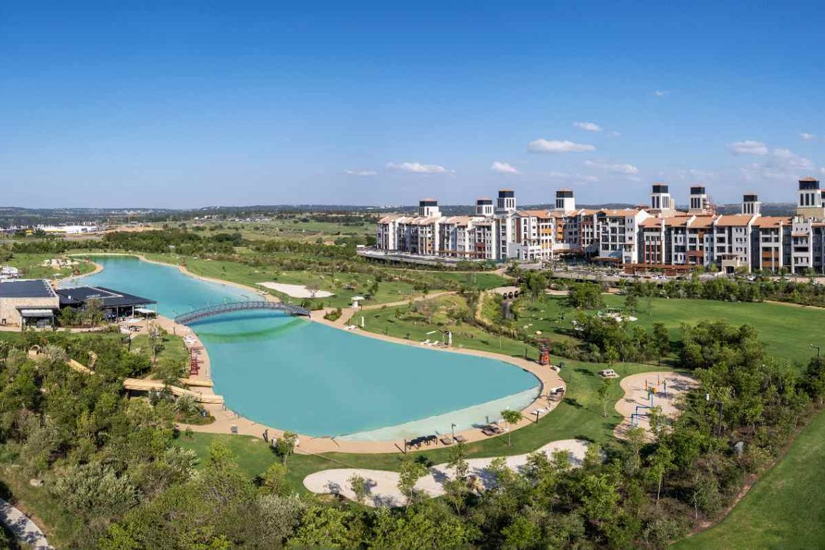 Aerial view of a large residential estate featuring a central lagoon, landscaped gardens, sports facilities, and multi-story apartment buildings.