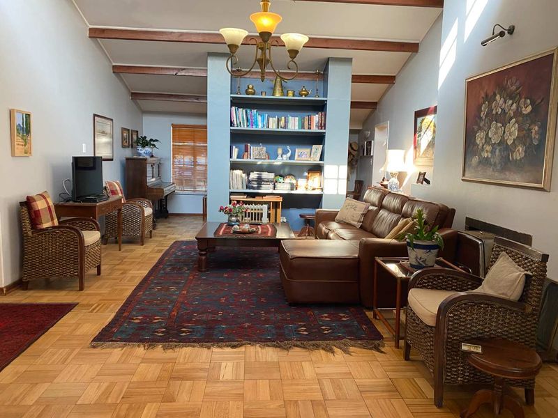 Spacious living room featuring classic parquet flooring, exposed timber ceiling beams, and a central built-in shelving unit, creating a warm and traditional atmosphere.