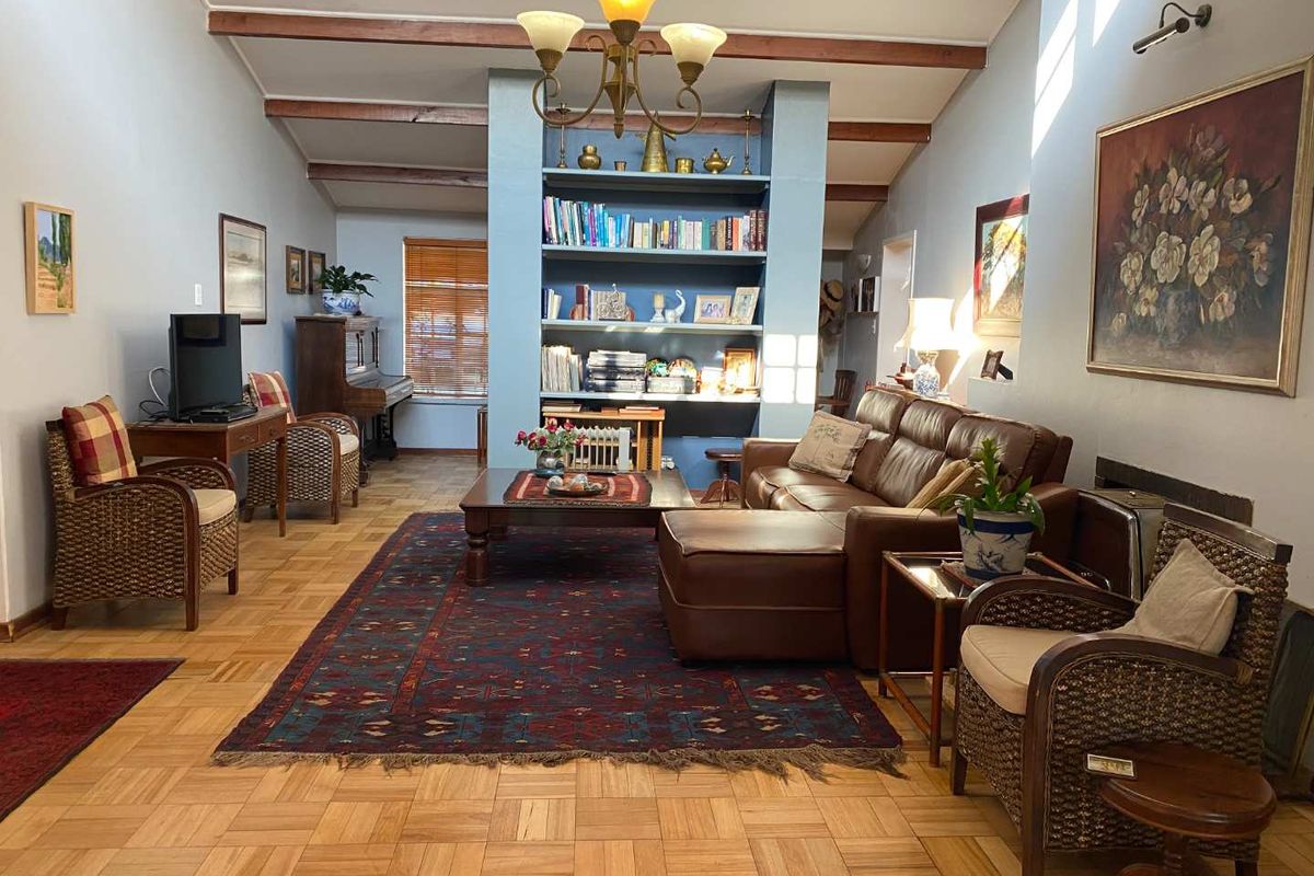 Spacious living room featuring classic parquet flooring, exposed timber ceiling beams, and a central built-in shelving unit, creating a warm and traditional atmosphere.