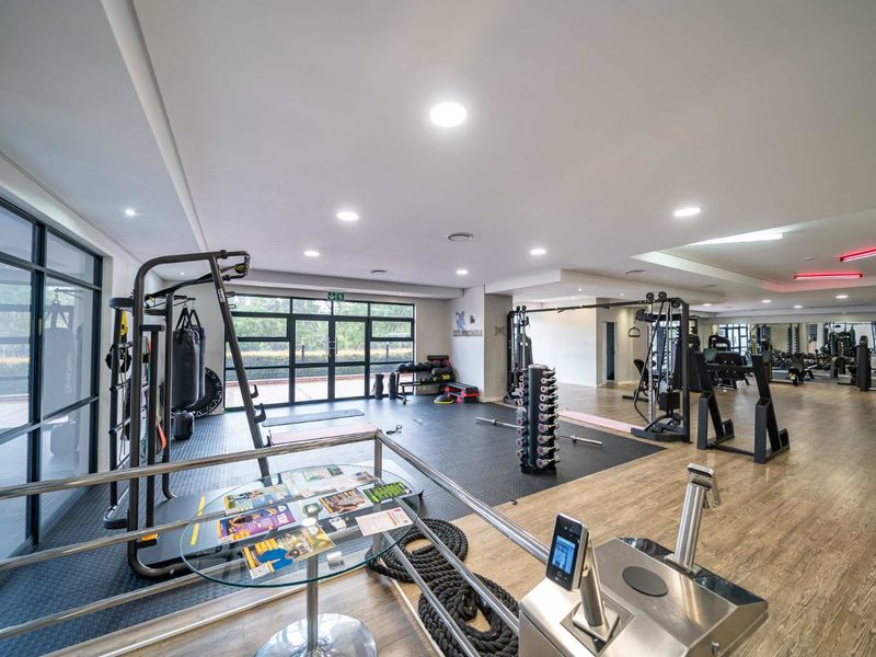 A spacious, well-lit gym facility featuring a mix of rubber and laminate flooring, large glass doors, and integrated recessed lighting.