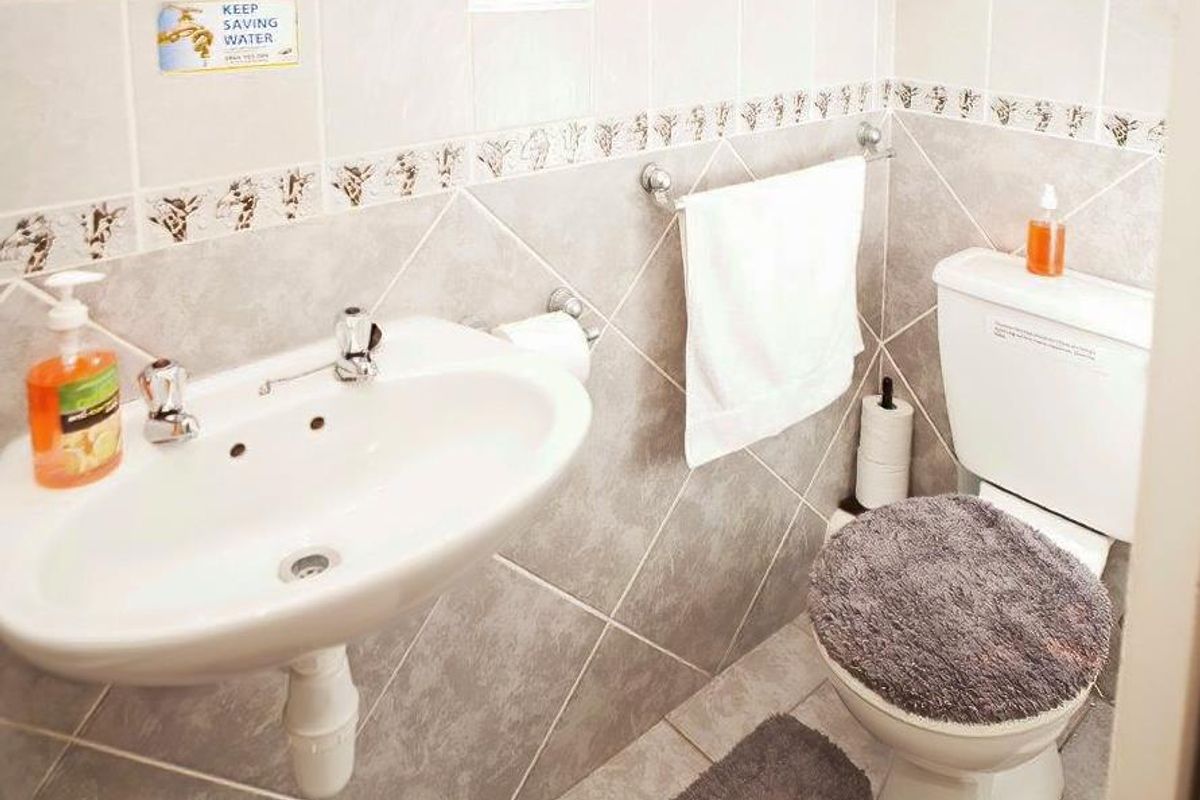 A compact bathroom featuring a pedestal basin, toilet, and neutral tiled finishes with decorative border detailing.