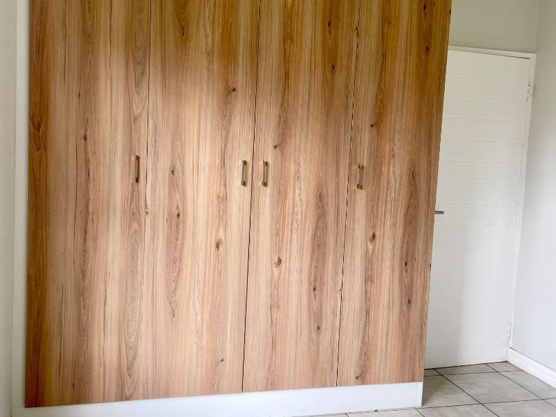 A clean, empty bedroom featuring modern wood-grain built-in wardrobes and neutral floor tiles, offering a versatile space ready for personalization.