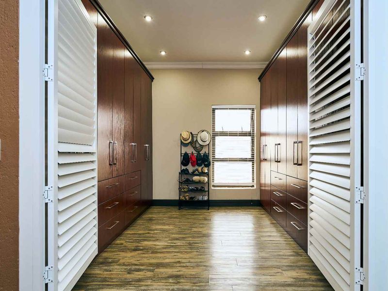 A well-appointed walk-in closet or dressing area featuring extensive dark wood built-in cabinetry, recessed lighting, and modern laminate flooring.