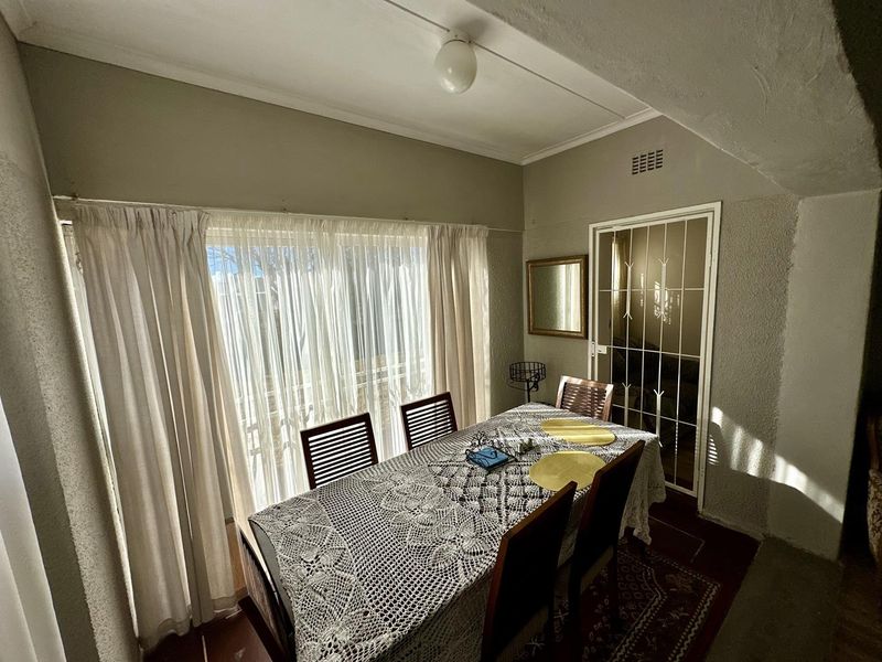 A functional dining room featuring a large window with curtain treatments and a secure internal door with a metal security gate.