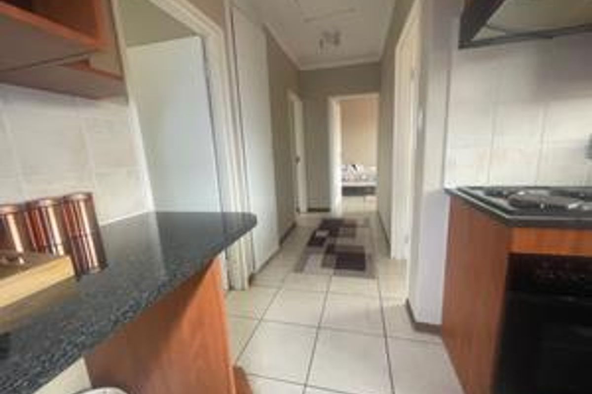 A functional kitchen featuring granite countertops, built-in cabinetry, a gas hob, and an integrated oven, leading into a tiled hallway.