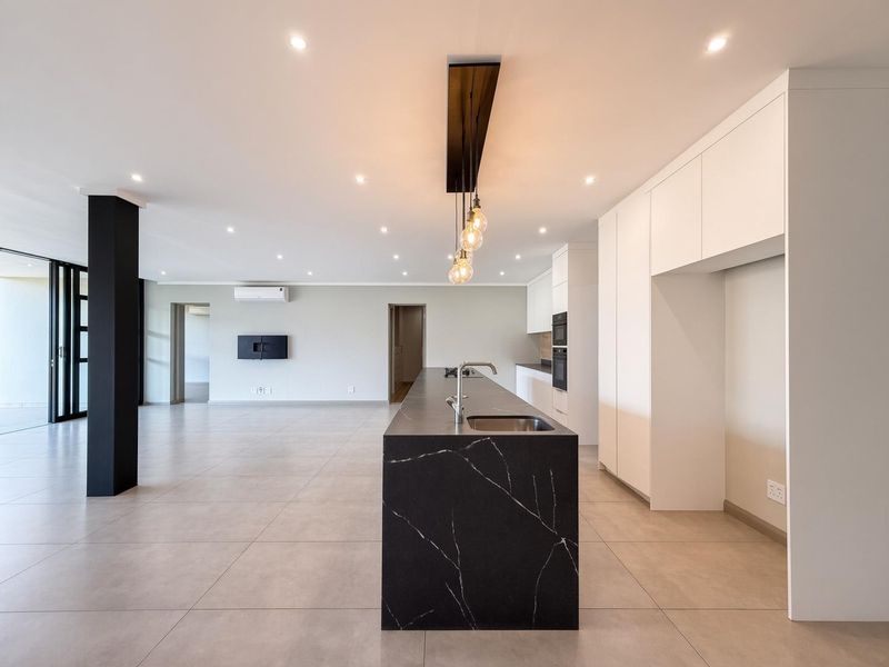 Spacious open-plan living and kitchen area featuring a modern black stone island, sleek white cabinetry, tiled floors, and recessed lighting throughout.