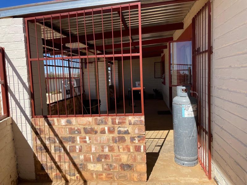 A covered outdoor patio area featuring brick walls, concrete flooring, and metal security gates, providing a functional utility or transition space.